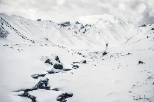 Un randonneur dans le val de Courre enneigé, le massif du Sancy dans les nuages.